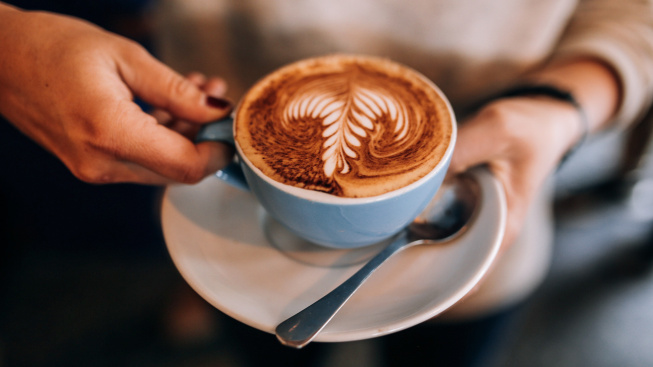 woman-holds-cup-saucer-with-hot-latte-coffee
